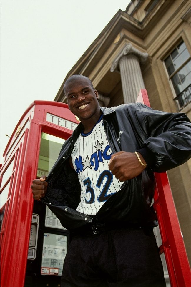 a man standing in front of a red phone booth with his hand on his hip