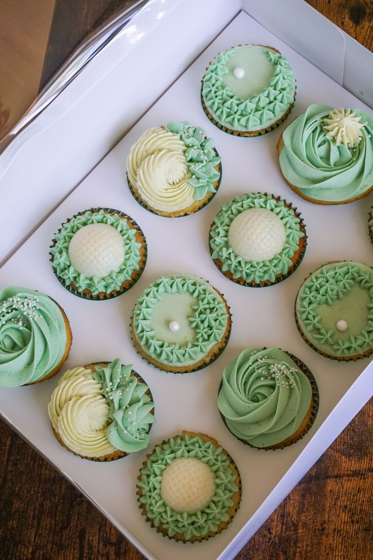 twelve cupcakes with green frosting in a white box on a wooden table