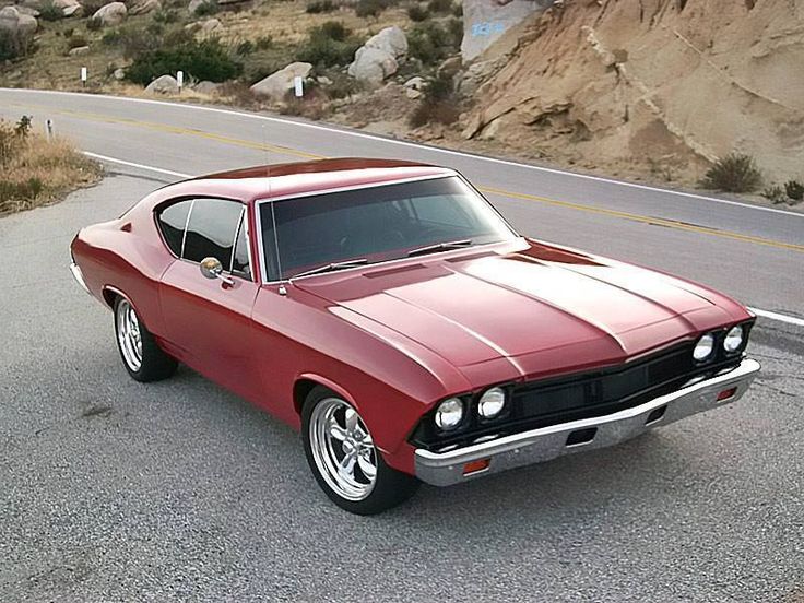 an old red car is parked on the side of the road in front of some rocks