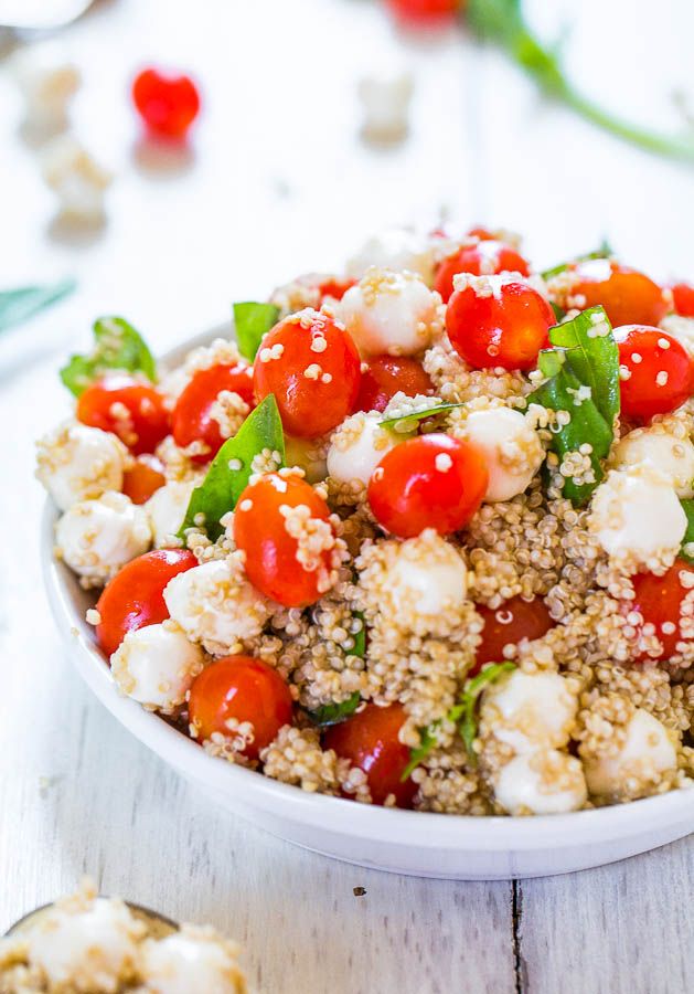 a white bowl filled with tomatoes and cauliflower next to two spoons on a table