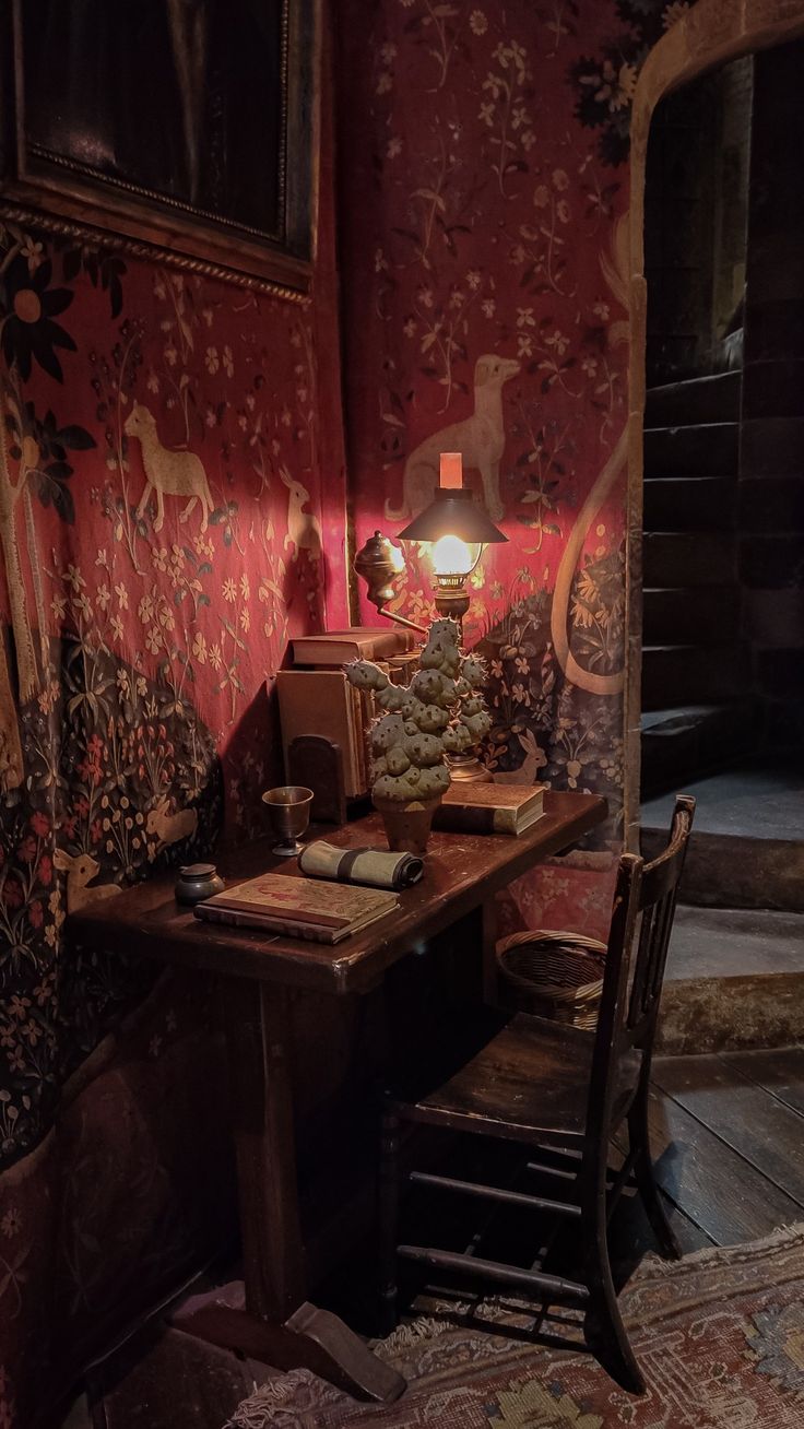 A Gryffindor common room study nook with a lamp and a mimbulus mimbletonia plant on the desk. Hogwarts Room Aesthetic, Mimbulus Mimbletonia, Harry Potter Common Room, Hogwarts Common Rooms, Plant Instagram, Dark Academia Desk, Christmas At Hogwarts, Hogwarts Room, Interior Paint Schemes