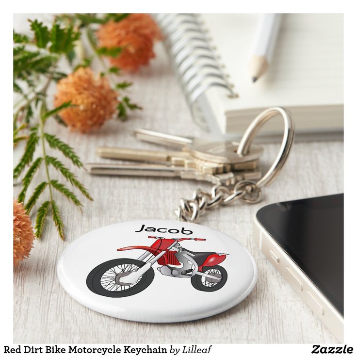 a red motorcycle keychain sitting on top of a table next to a cell phone