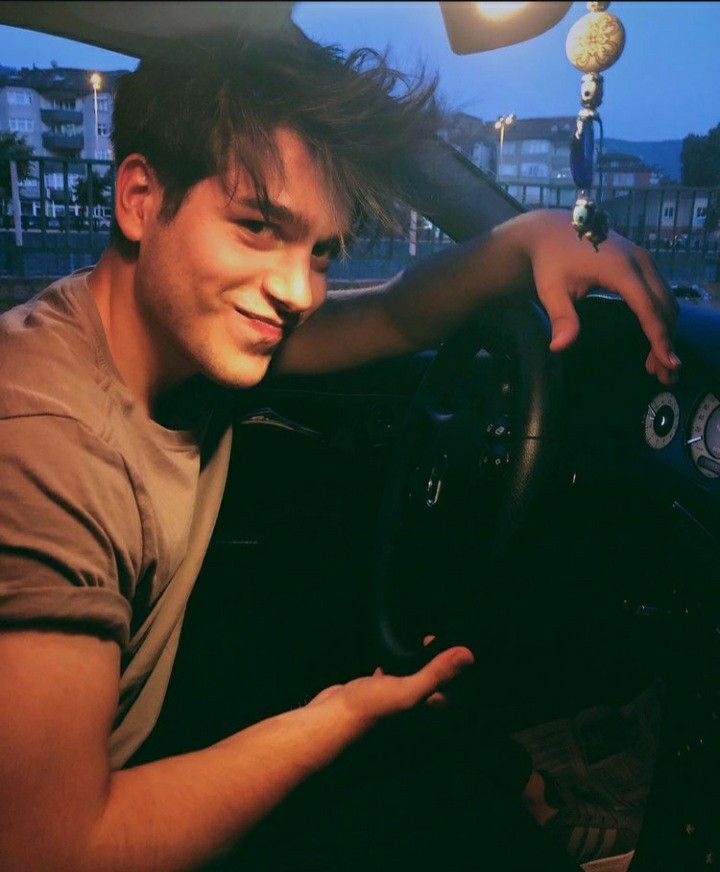 a man sitting in the driver's seat of a car with his hand on the steering wheel