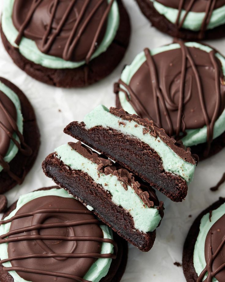 chocolate cookies with mint green cream frosting are on a white surface and one is cut in half