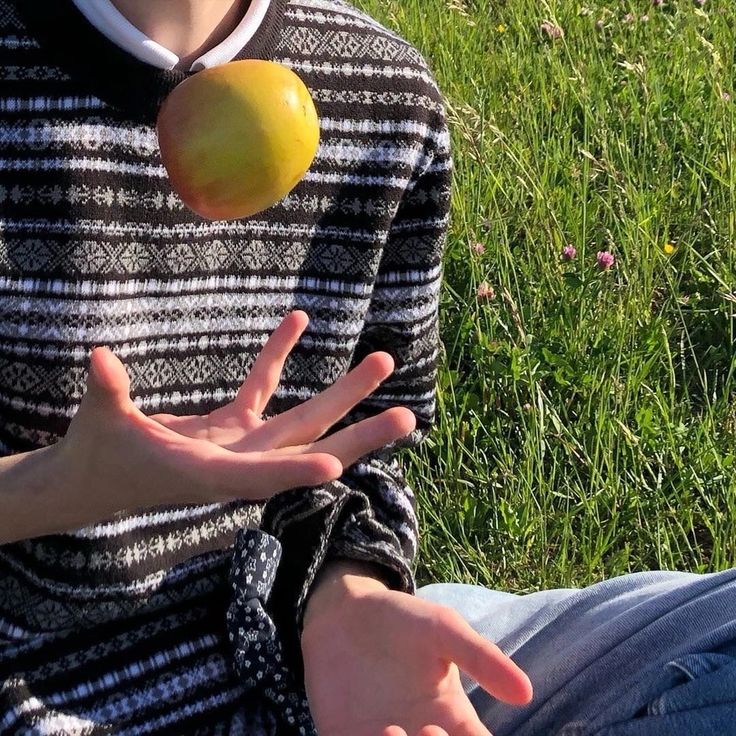 a person sitting in the grass with an apple on his hand and another hand reaching out for it