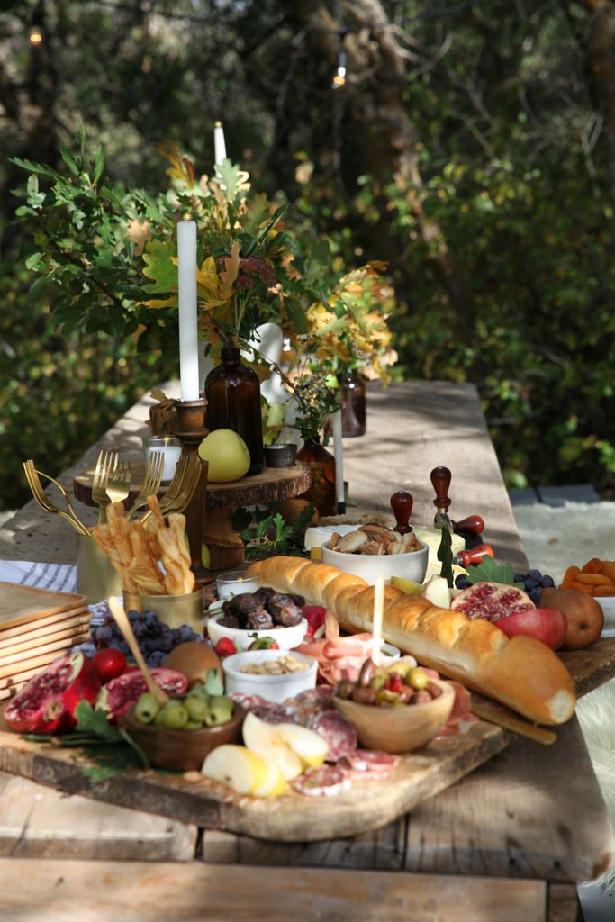 an outdoor table with food and candles on it, including breads, grapes, apples, and other foods