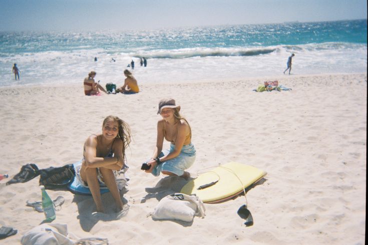 two women sitting on the beach with their surfboards