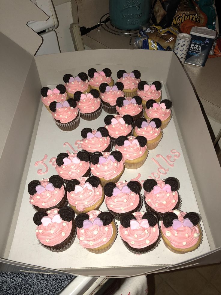 a box filled with lots of cupcakes covered in pink and black frosting