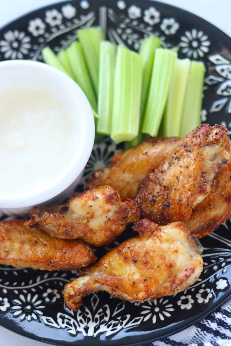 chicken wings with celery and ranch dressing on a black plate, ready to be eaten