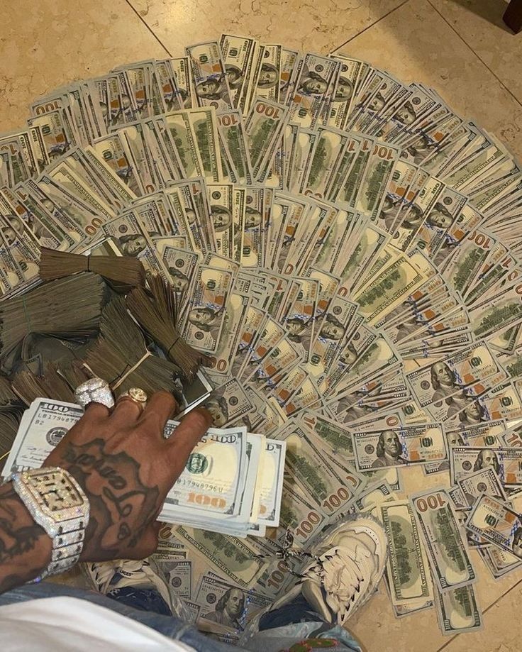 a person sitting on the floor with stacks of money in front of him and his hand