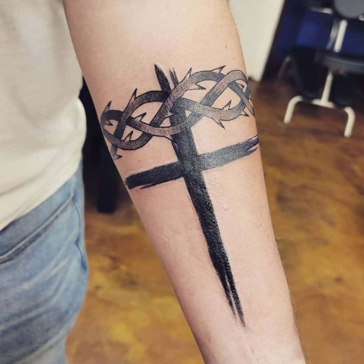 a cross tattoo on the arm with an arrow