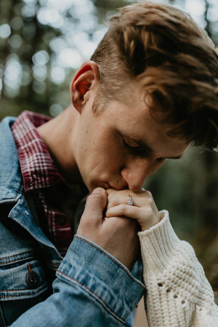 a man with his hand on his face and wearing a sweater in front of trees