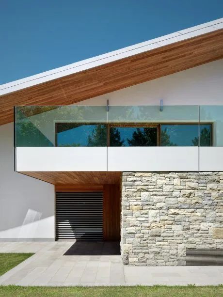 a modern house with glass railings and stone wall on the front porch, along with an open garage door