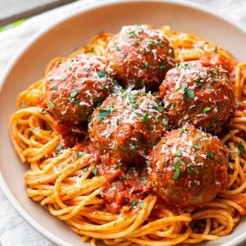 spaghetti and meatballs are served in a white bowl