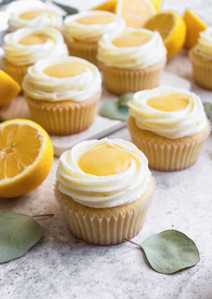 lemon cupcakes with white frosting and sliced lemons on the side next to them