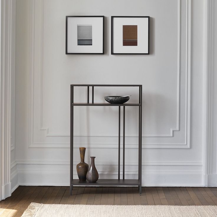 two vases are sitting on a shelf in front of a wall with framed pictures