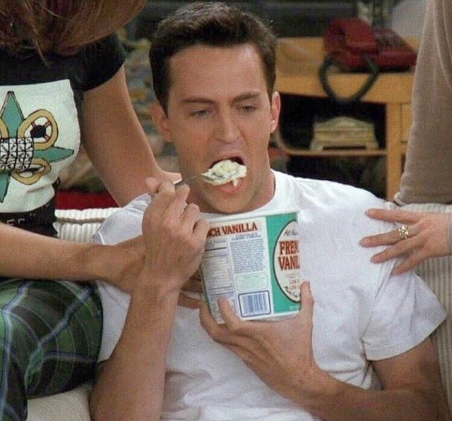 a man sitting on a couch holding a box of cereal with his mouth covered in marshmallows