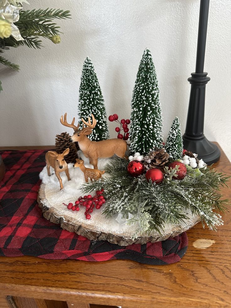 a christmas scene on a table with deer, pine trees and other holiday decor items