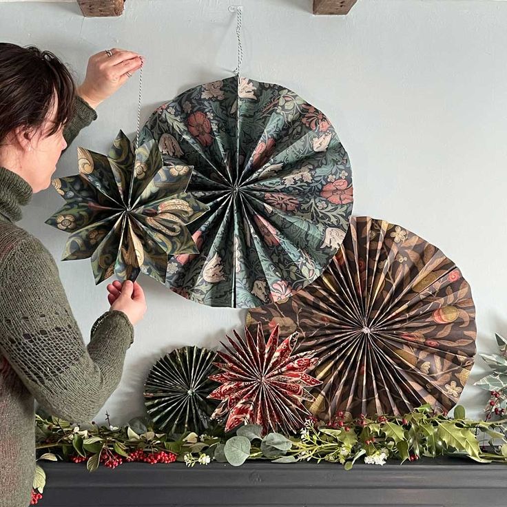 a woman is looking at paper fans hanging on the wall next to a mantel