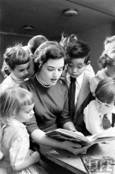 an old black and white photo of children looking at a book while adults look on