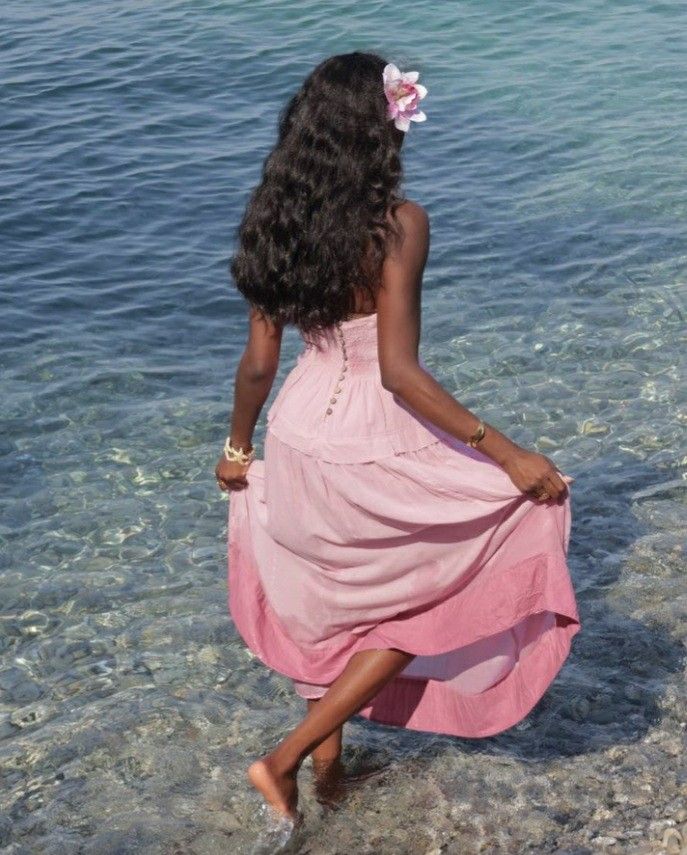 a woman in a pink dress walking into the water