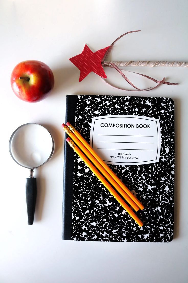 an apple, magnifying glass and composition book