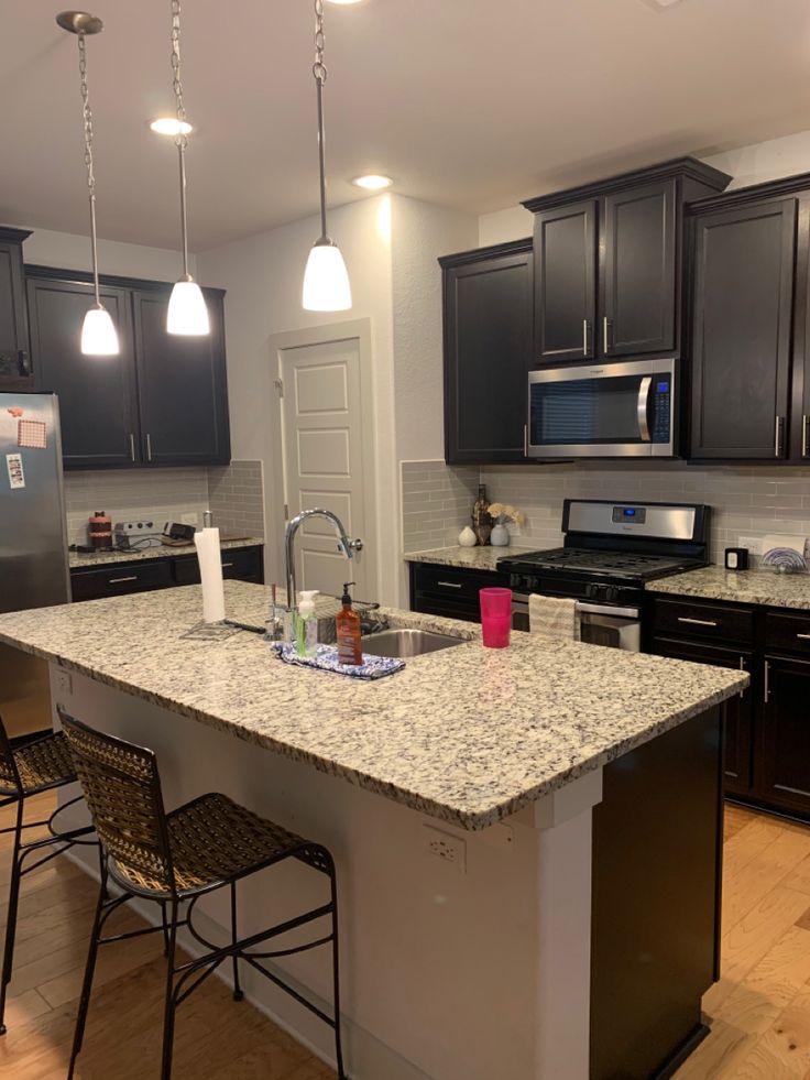 a kitchen with black cabinets and granite counter tops, an island in the middle is surrounded by bar stools