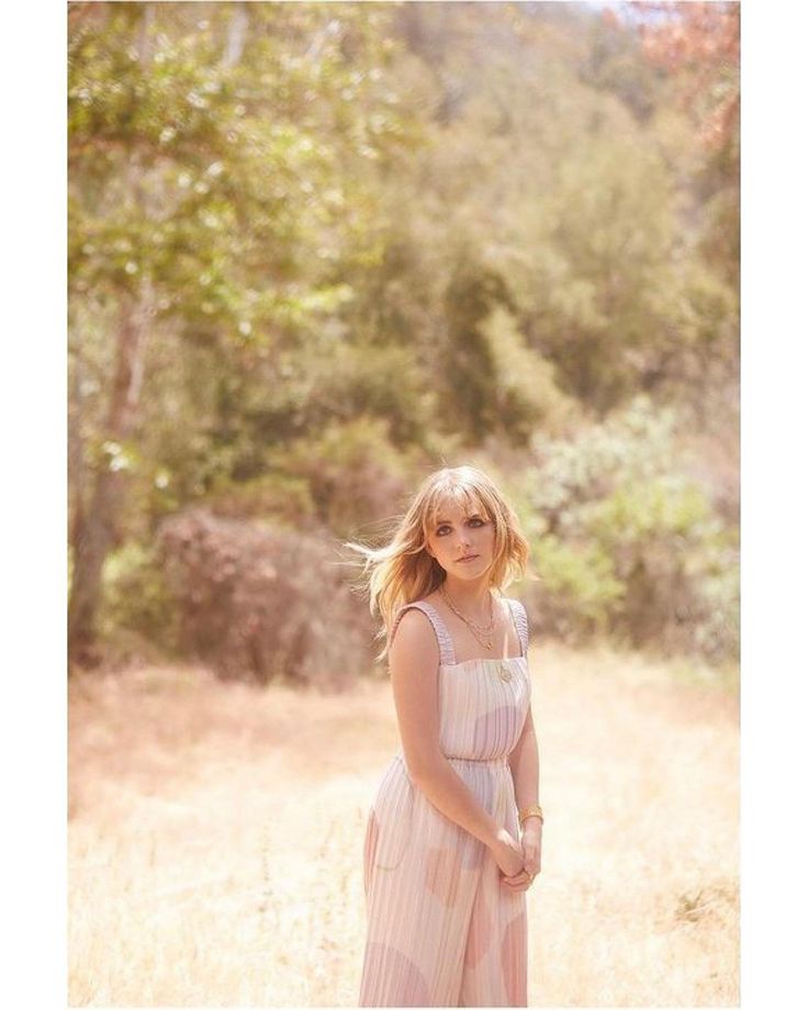 a woman in a pink dress is standing in the grass and looking at the camera