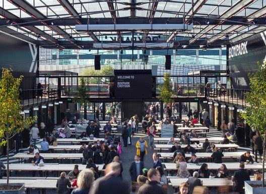 people are sitting at tables in an open air area with lots of windows and plants