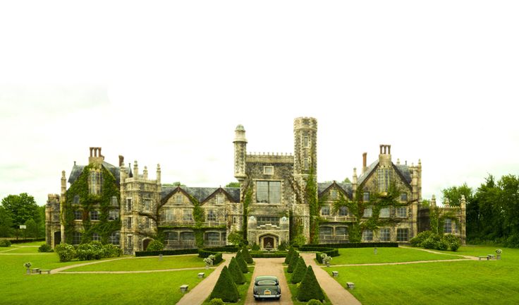 a car is parked in front of a large building with hedges and trees on both sides