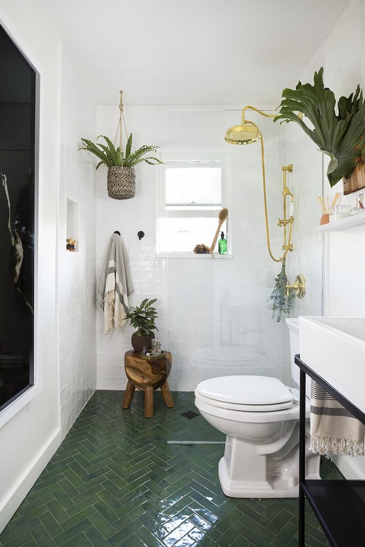 a white toilet sitting in a bathroom next to a green tiled floor with plants on the wall