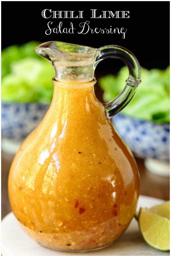 a glass carafe filled with sauce on top of a white plate next to limes and lettuce