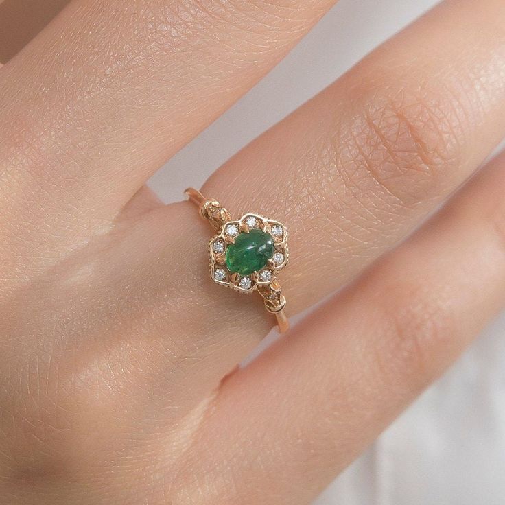 a woman's hand with a green ring on top of her finger and an emerald stone in the middle