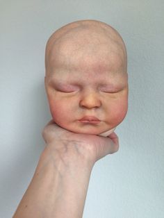 a hand holding a baby doll with it's head resting on its arm and eyes closed