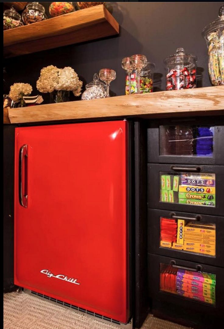 a red refrigerator sitting in the middle of a kitchen next to shelves filled with candy