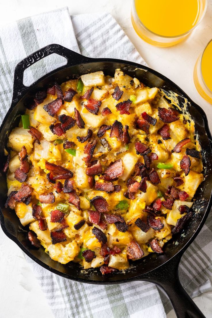 a skillet filled with potatoes and bacon next to two glasses of orange juice