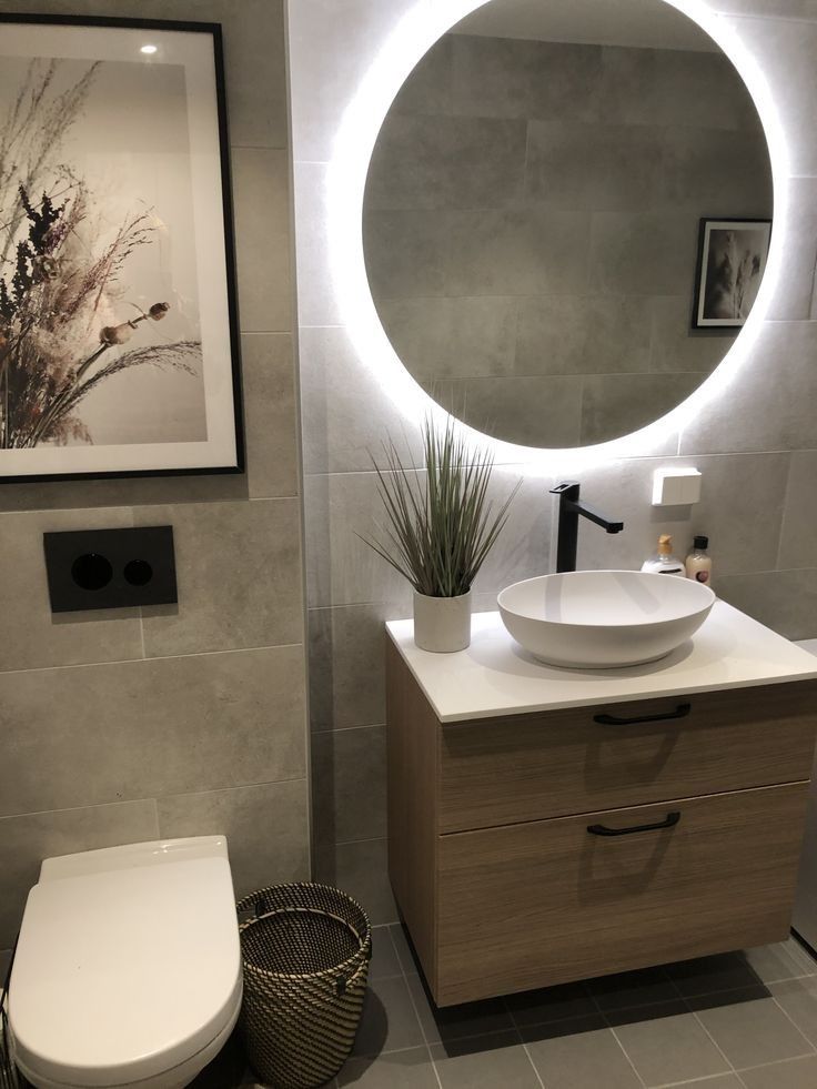 a white toilet sitting next to a bathroom sink under a round mirror on a wall