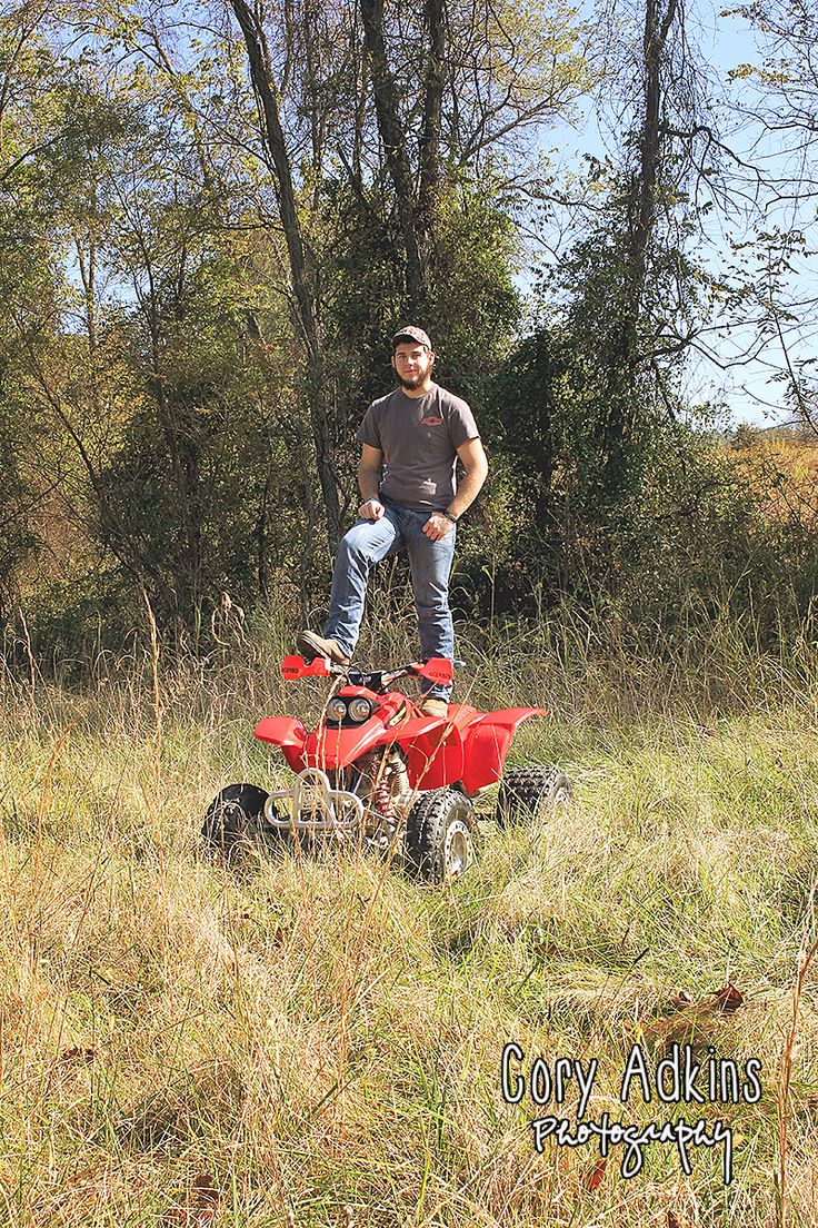 a man riding on the back of an atv in a field with trees behind him