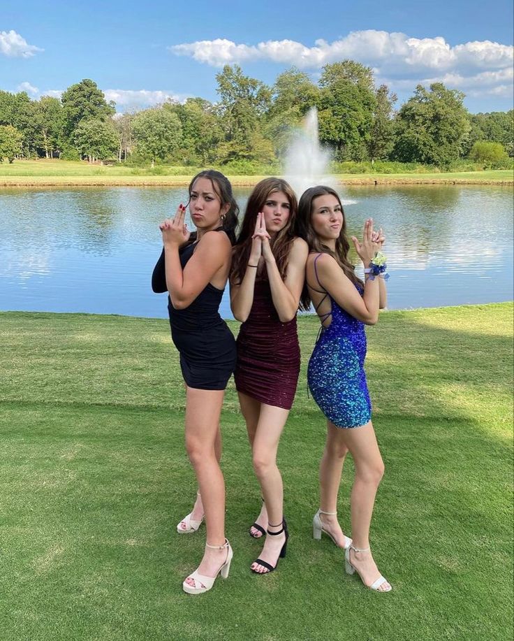 three young women standing in front of a pond posing for the camera with their hands together