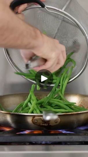 someone using a strainer to stir green beans in a frying pan