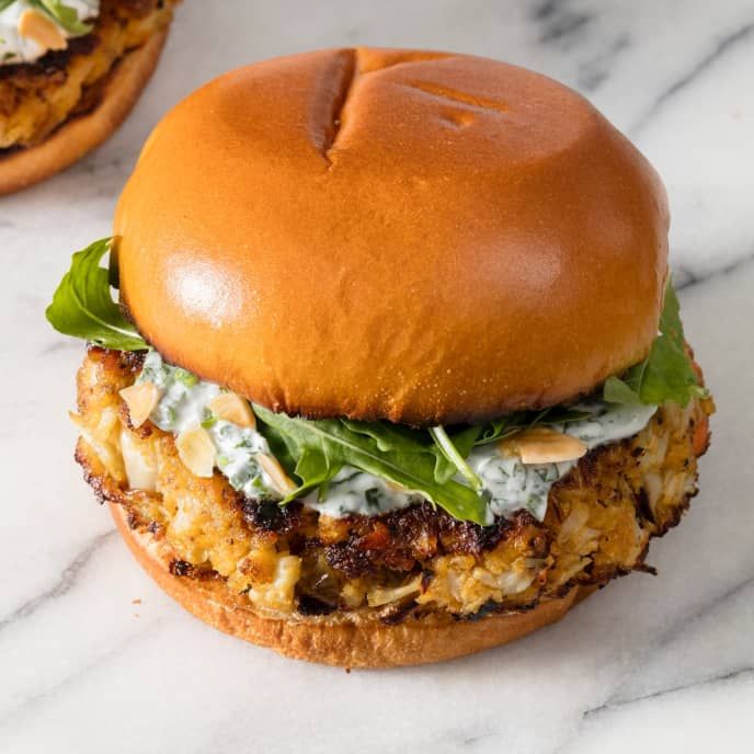 two burgers with meat, lettuce and sauce on them sitting on a marble surface