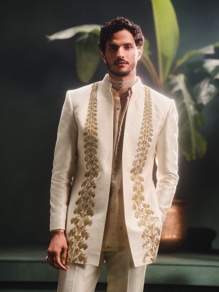 Step into refined elegance with the Kaju Katli Raja koti, an opulent sherwani adorned with intricate gold zardozi, katdana, and pearl embroidery, inspired by 'Berry Bel'. The ensemble includes a short georgette tissue kurta that adds a playful touch and straight, tailored pants for a smart finish. This piece is a perfect blend of grandeur and modern sophistication. Reception Nehru Jacket With Resham Embroidery And Traditional Drape, Nehru Jacket With Resham Embroidery For Reception, Designer Bandhgala With Intricate Embroidery In Chanderi, Designer Chanderi Bandhgala With Intricate Embroidery, Elegant White Chanderi Nehru Jacket, Chanderi Bandhgala With Traditional Drape For Designer Wear, Bollywood Style Off White Traditional Wear With Gota Work, Gold Kurta With Gota Work For Transitional Season, Designer Wear Semi-stitched Chanderi Nehru Jacket