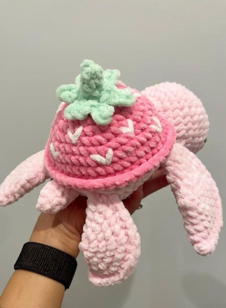 a hand holding a pink crocheted stuffed animal with a green flower on top