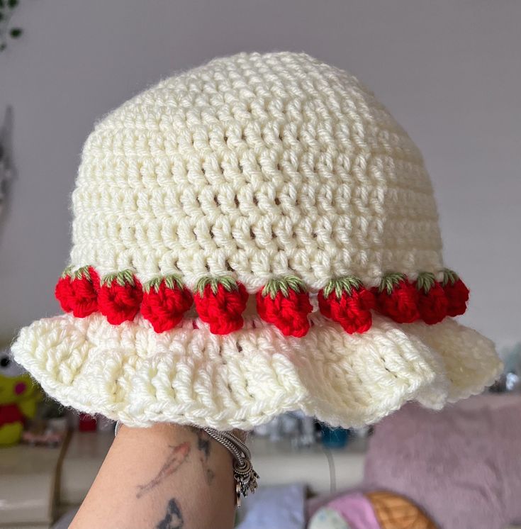 a white crocheted hat with red flowers on the brim and bottom part