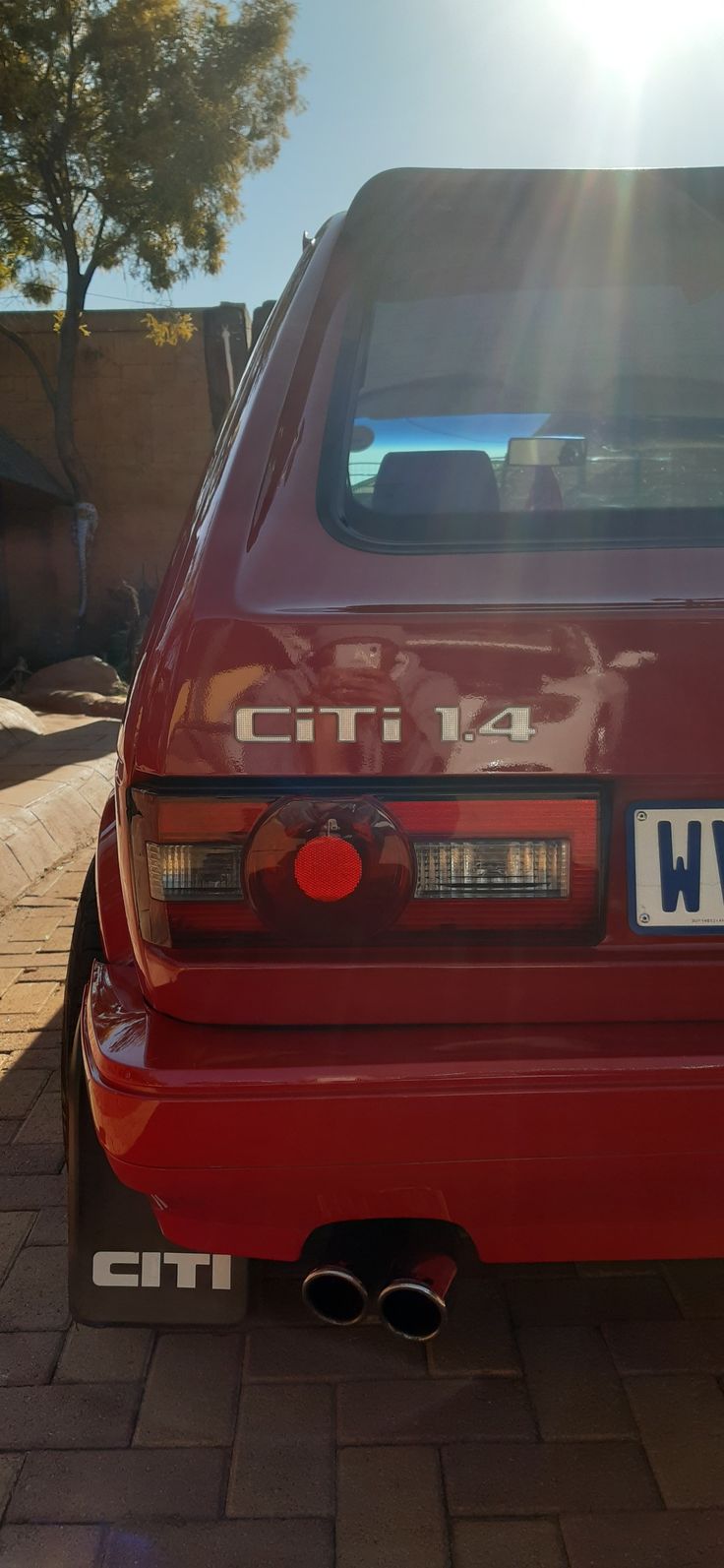 the back end of a red car parked on a brick road