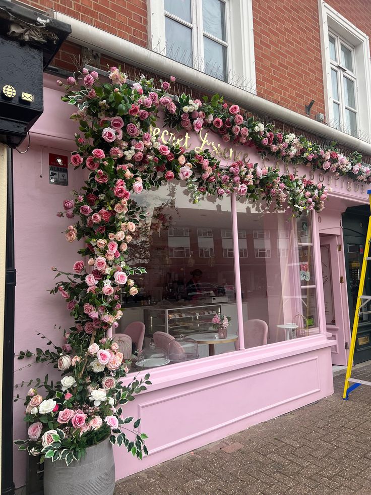 a pink store front with flowers on the window and ladders in front of it