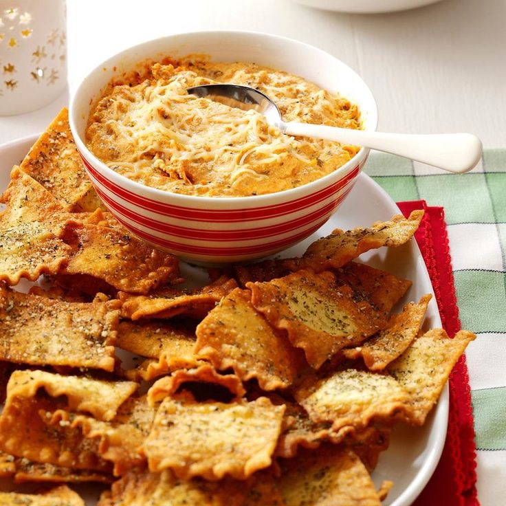 a bowl of dip surrounded by tortilla chips on a red and white plate