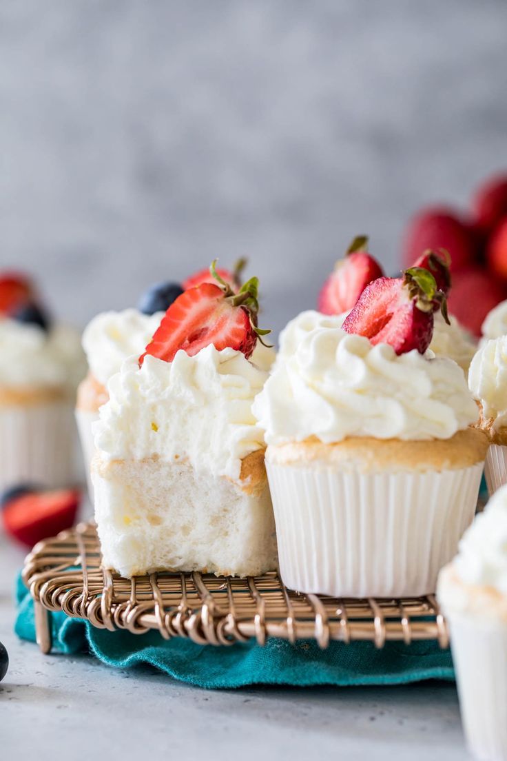 several cupcakes with white frosting and fresh strawberries on top, sitting on a wicker tray