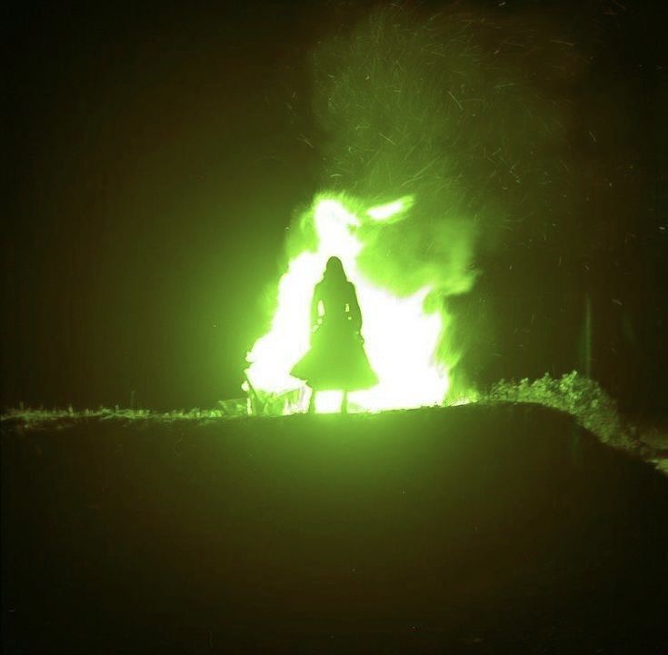 a woman standing in front of a fire with bright green lights on her face and arms