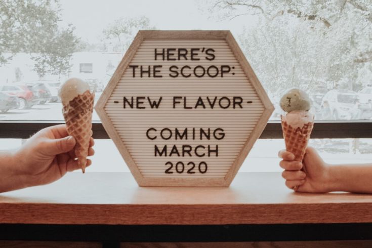 two people holding ice cream cones in front of a sign that says here's the scoop new flavor coming march